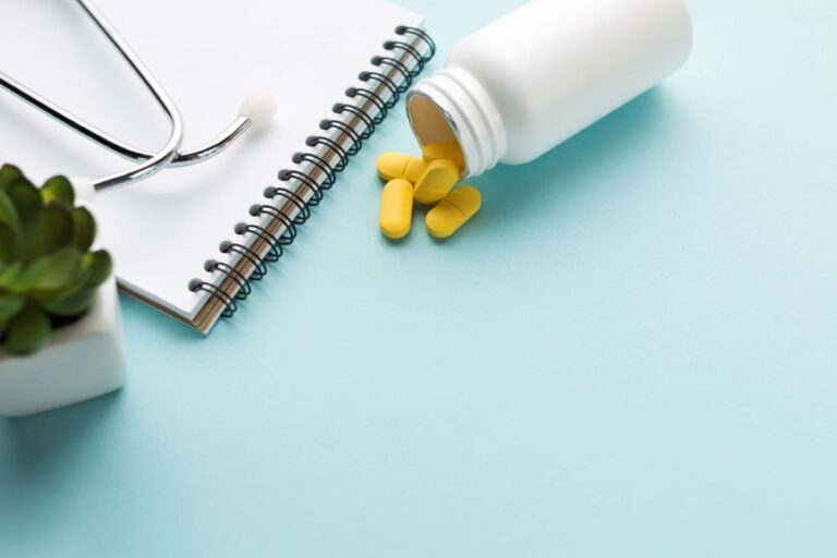 stethoscope spiral notepad near yellow pills spilled front white bottle blue backdrop 768x512
