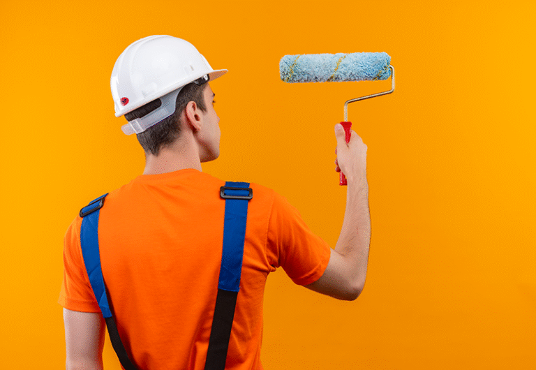 optimiz young builder man wearing construction uniform safety helmet paints wall with roller brush 768x530